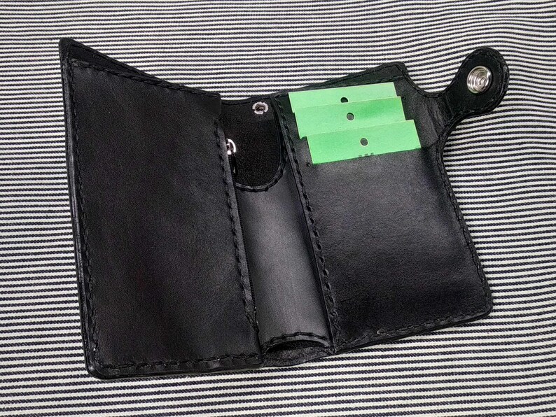 May include: A black leather wallet with multiple card slots and a snap closure. The wallet has a small pocket on the outside for a key or other small item.