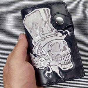 May include: Black leather wallet with a tooled design of a skull wearing a top hat and a rose.