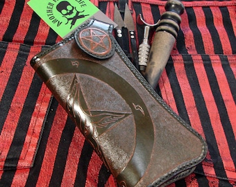May include: A brown leather wallet with a pentagram design and a stitched border. The wallet is lying on a black and red striped fabric.