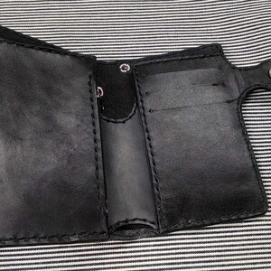 May include: A black leather wallet with multiple card slots and a flap closure. The wallet has a stitched edge and a silver snap closure.