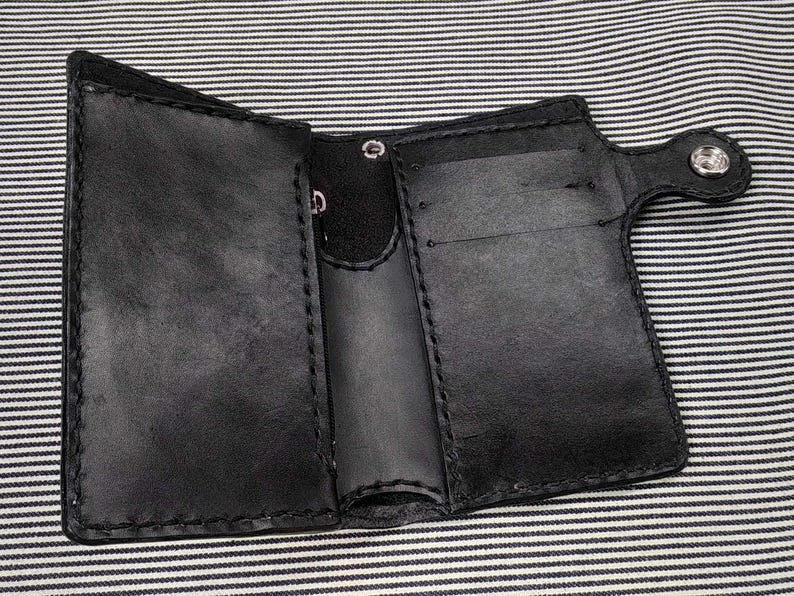 May include: A black leather wallet with multiple card slots and a flap closure. The wallet has a stitched edge and a silver snap closure.