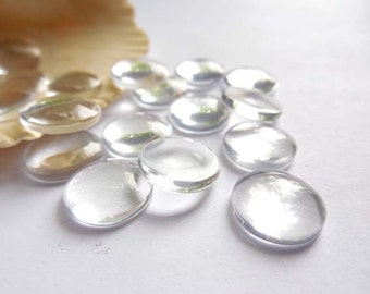 May include: A pile of clear glass gems, resembling pebbles, scattered on a white surface. The gems are smooth and round, with a slight shine.
