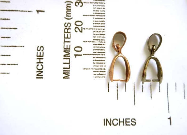 May include: Two metal pendant bails, one gold and one silver, are shown next to a ruler. The bails are about 1 inch long.
