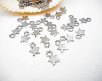 Puede incluir: Una dispersión de dijes en forma de estrella plateados con anillos de salto. Los dijes están sobre una superficie blanca.