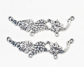 May include: Two silver-toned metal grape vine charms. Each charm features a cluster of grapes, leaves, and a curved stem with loops for attaching to other components. Ideal for jewelry making or craft projects.