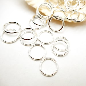 May include: A group of silver jump rings, a type of jewelry finding, scattered on a white surface. The rings are of various sizes and are perfect for connecting jewelry components.