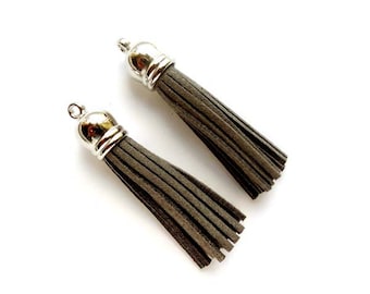 May include: Two gray suede tassels with silver metal tops. The tassels are about 2 inches long.