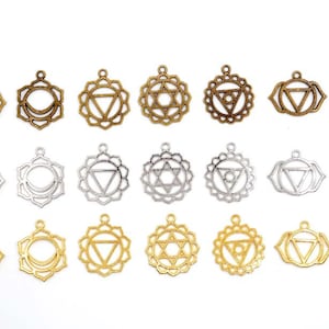 May include: A set of 18 silver and gold metal charms featuring the seven chakra symbols, including the root, sacral, solar plexus, heart, throat, third eye, and crown chakras. The charms are in the shape of a mandala with a flower design.