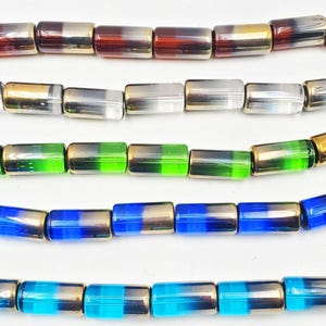 May include: Close-up of several strands of colorful beads. The beads are rectangular with metallic gold ends and a translucent center in shades of red, clear, green, blue, and turquoise. The beads are strung together, creating a vibrant display.