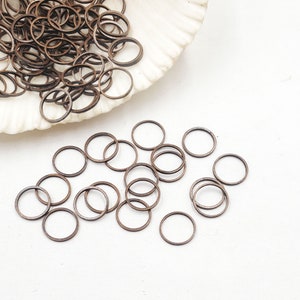 May include: A pile of small, round, copper-coloured jump rings. The rings are scattered on a white surface.