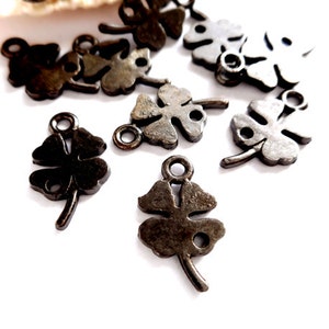 May include: A group of 12 black metal four-leaf clover charms with a loop at the top for attaching to jewelry or crafts.