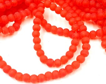 May include: Close-up of strands of bright red beads. The beads are small, round, and have a matte finish. The beads are strung together, creating a flowing, organic pattern against a white background. Ideal for jewelry making.
