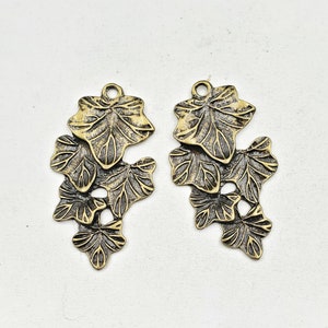 May include: Two antique gold-toned metal charms shaped like clusters of ivy leaves.
