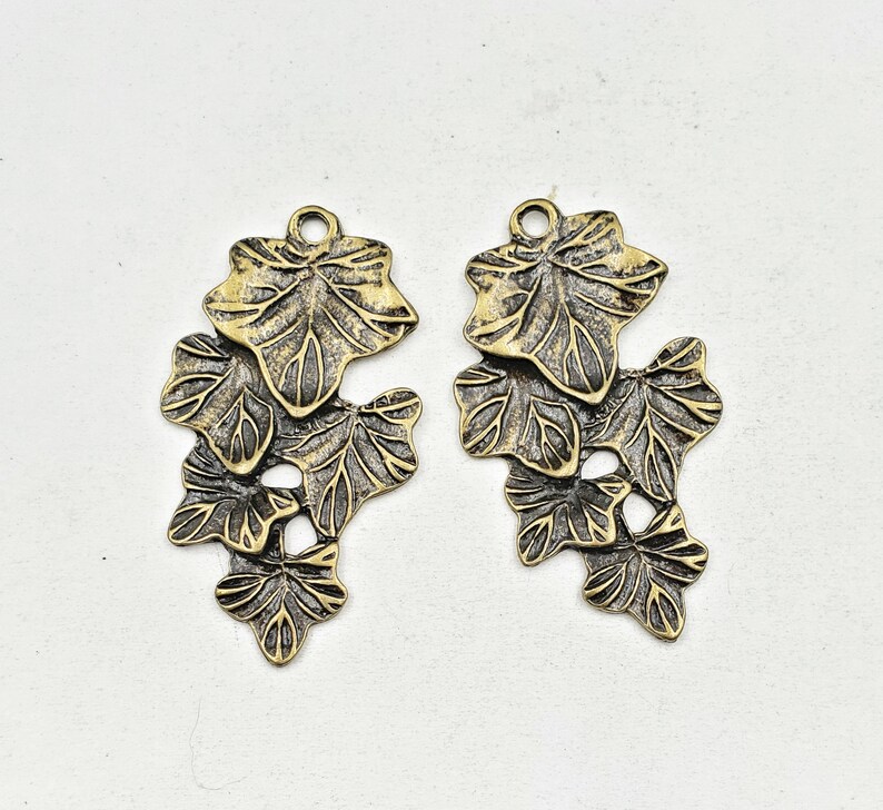 May include: Two antique gold-toned metal charms shaped like clusters of ivy leaves.