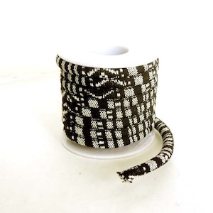May include: A spool of black and white patterned cord. The cord is wound around a white plastic spool.