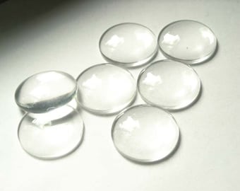 May include: Seven clear glass cabochons, round and smooth, with a slightly domed shape. The cabochons are arranged in a semi-circle on a white surface.