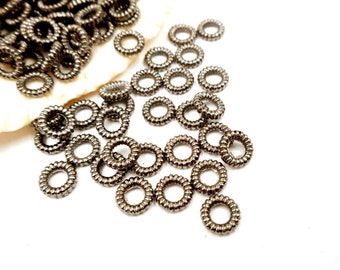 May include: A pile of silver-toned metal rings, each with a coiled design. The rings are scattered on a white surface.