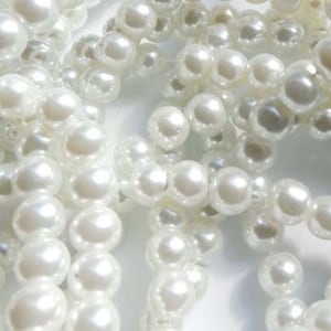 May include: A close-up of a pile of white pearl beads. The beads are round and smooth, and they are arranged in a random pattern.