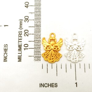 May include: Two angel charms, one gold and one silver, with intricate designs. The charms are about 1 inch tall and are shown next to a ruler.