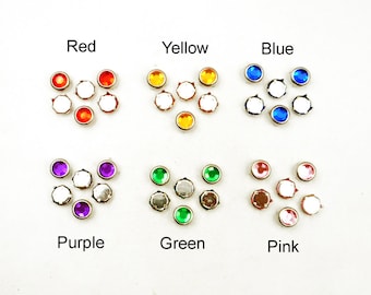 May include: Assortment of colorful rhinestones in red, yellow, blue, purple, green, and pink. Each color is arranged in a small cluster of seven rhinestones.