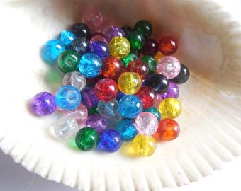May include: A collection of colorful glass beads in various shades of red, orange, yellow, green, blue, purple, and clear. The beads are round and have a slightly iridescent finish.