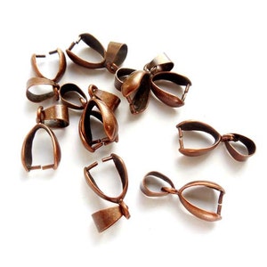 May include: A group of ten copper-colored metal pendant bails. The bails are oval-shaped with a small loop at the top for attaching a pendant.