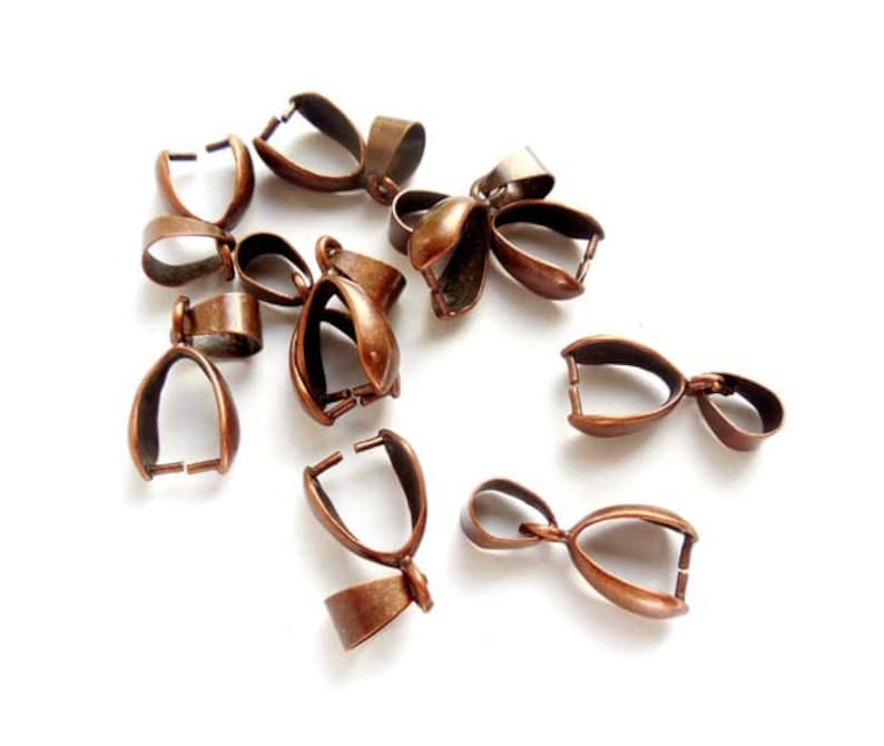 May include: A group of ten copper-colored metal pendant bails. The bails are oval-shaped with a small loop at the top for attaching a pendant.