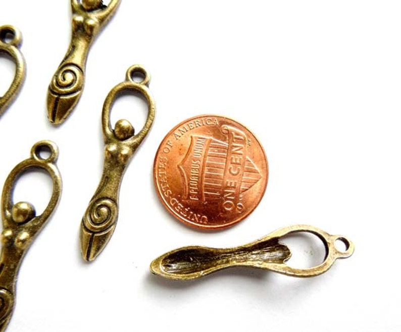 May include: Antique bronze charms featuring a stylized female figure with a spiral design. The charms are approximately the size of a US penny.