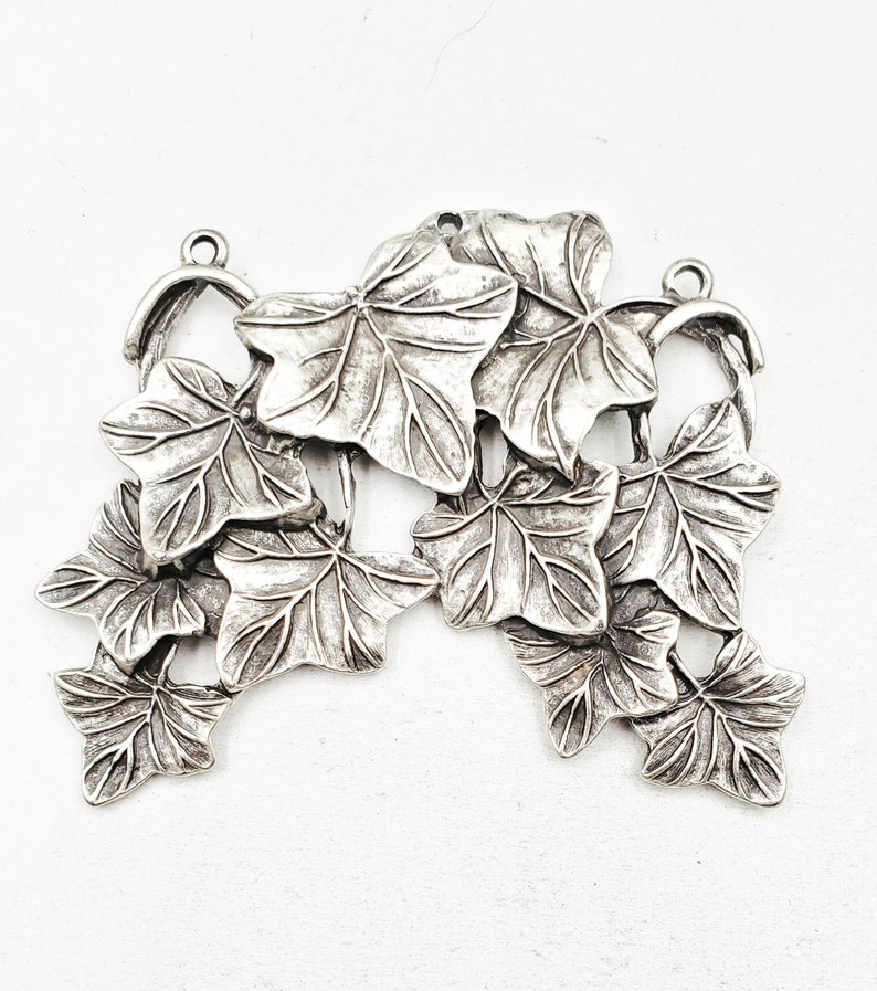 May include: Silver-toned metal charm featuring a cluster of ivy leaves. The leaves are detailed and realistic, with a textured surface.