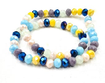 May include: A strand of faceted round beads in a multi-colored pattern featuring shades of bright yellow, deep royal blue, light sky blue, soft cream, and muted grey. The beads are arranged in a continuous loop, showcasing a reflective surface.
