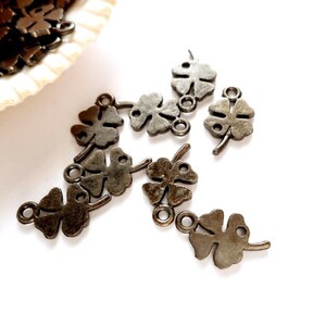 May include: A group of ten antique silver-toned four-leaf clover charms with a loop for attaching to jewelry or other crafts.