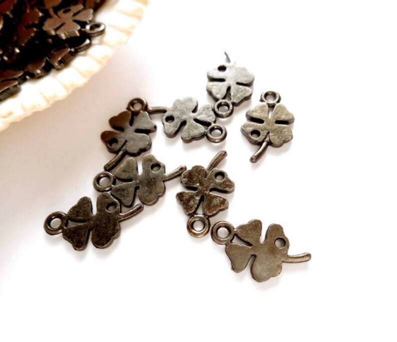 May include: A group of ten antique silver-toned four-leaf clover charms with a loop for attaching to jewelry or other crafts.