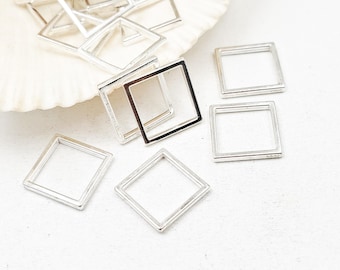 May include: A collection of small, silver-colored square frames. Some are scattered on a white surface, while others rest on a seashell. The frames have a simple, open design, with clean lines and a metallic sheen. They appear to be jewelry components or craft supplies.