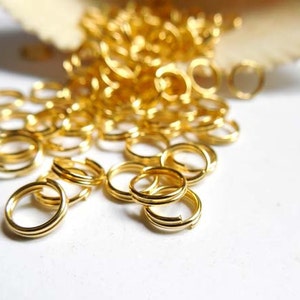 May include: A pile of gold jump rings, a type of jewellery finding, on a white surface. The rings are small and delicate, and they are perfect for making jewellery.