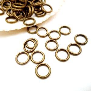 May include: A pile of small, gold-colored metal jump rings. The rings are scattered on a white surface.