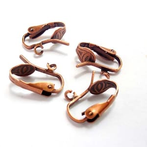 May include: Four copper-colored earring clips with a decorative design. The clips are made of metal and have a spring-loaded mechanism.