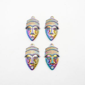 May include: Four iridescent metal charms shaped like African masks with intricate details. Each charm features a gold-colored face with a black and white patterned design and a beaded headdress.