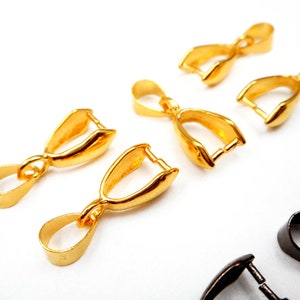 May include: Five gold-toned metal pendant bails, each with a loop at the top and a curved opening at the bottom. The bails are arranged in a semi-circle on a white surface.