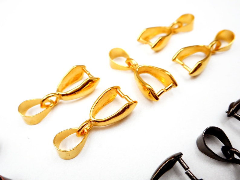 May include: Five gold-toned metal pendant bails, each with a loop at the top and a curved opening at the bottom. The bails are arranged in a semi-circle on a white surface.