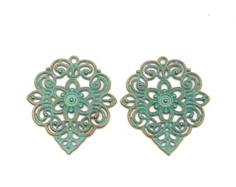 Puede incluir: Dos encantos de metal adornados con un acabado azul verdoso y un contorno dorado. Los encantos presentan un diseño floral con detalles intrincados.