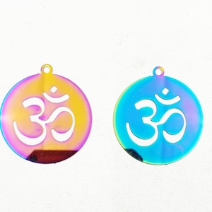 May include: Two iridescent metal charms with an Om symbol cut out. The charm on the left is a yellow-pink color, and the charm on the right is a blue-green color.