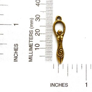 May include: A gold-toned metal charm depicting a stylized female figure with a spiral design. The charm is approximately 1 inch in length and is shown next to a ruler for size reference.