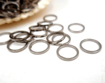 May include: A pile of silver jump rings, scattered on a white surface. The rings are small and round, with a smooth finish.