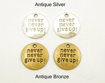 May include: Four round metal charms with the words "never never give up!" in black lettering. Two charms are antique silver and two are antique bronze.