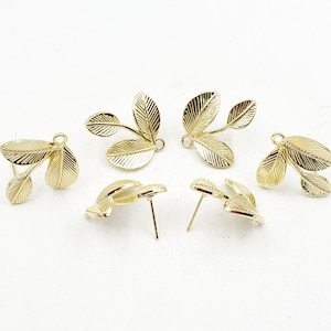 May include: Gold-colored leaf earrings. The earrings feature a delicate design of three leaves, with detailed veining. The earrings are shown on a white background. The earrings are post-style.