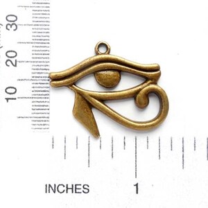 May include: A bronze-colored metal charm in the shape of the Eye of Horus, an ancient Egyptian symbol. The charm is about 1 inch long and has a loop at the top for attaching to a necklace or bracelet.