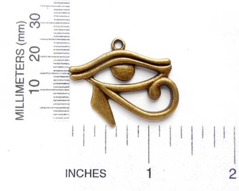 May include: A bronze-colored metal charm in the shape of the Eye of Horus, an ancient Egyptian symbol. The charm is about 1 inch long and has a loop at the top for attaching to a necklace or bracelet.