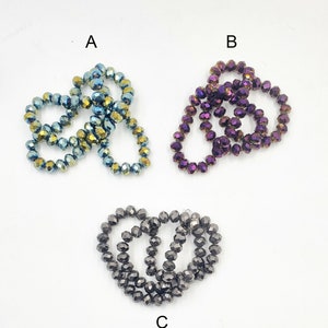 Könnte beinhalten: Drei Stränge irisierender Glasperlen in Blau, Lila und Schwarz. Die Perlen sind facettiert und haben einen metallischen Glanz.