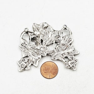 May include: Silver tone metal pendant charm with a floral design. The charm is made of three connected pieces, each with a detailed, textured pattern. The charm is about the size of a US penny.