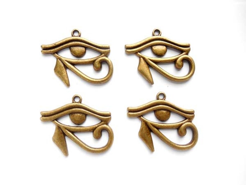 May include: Four antique gold-colored metal charms in the shape of the Eye of Horus, an ancient Egyptian symbol of protection.